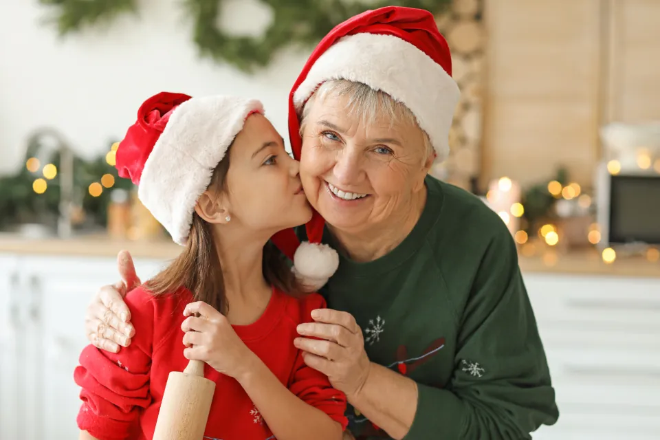 Niña con gorro de Papá Noel besando a su abuela en una cocina decorada para Navidad