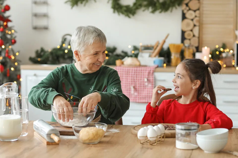 Abuela y nieta con suéteres navideños preparando masa de galletas en la cocina