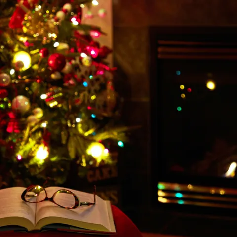 Libro abierto frente a la chimenea y el árbol de Navidad iluminado