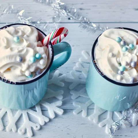 Dos tazas de chocolate caliente con malvaviscos y bastones de caramelo
