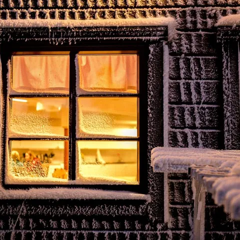 Ventana iluminada de una cabaña cubierta de nieve